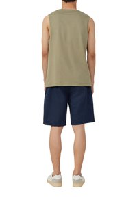 Olivgrünes ärmelloses Shirt, kombiniert mit marineblauen Shorts, die einen lässigen Schnitt und minimale Details aufweisen, abgerundet mit weißen Sneakers.