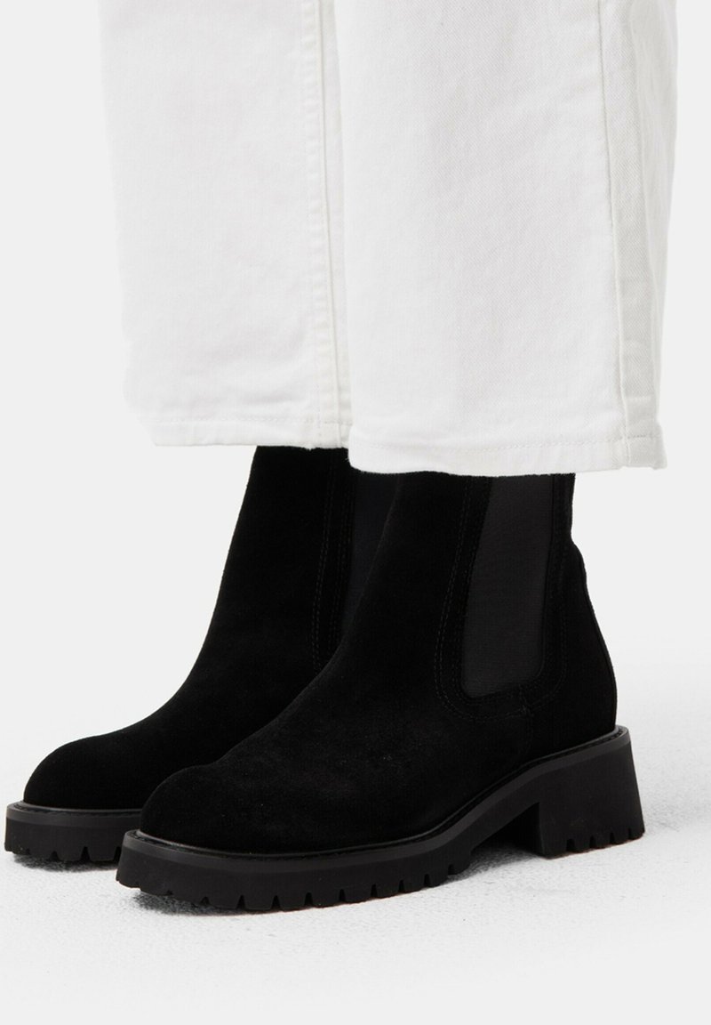 Black suede ankle boots with elastic side panels and a chunky rubber sole, featuring a textured finish and a slight heel.