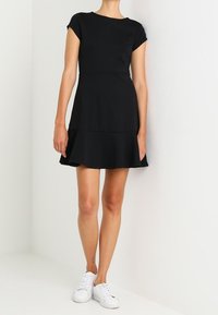 Czarna sukienka krótki rękaw z dopasowanym topem i rozszerzanym dołem, wykonana z gładkiego materiału. W połączeniu z białymi trampkami dla kontrastu.