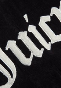 Κοντινό πλάνο λευκών υφασμάτινων γραμμάτων ραμμένων σε μαύρο υφή ύφασμα, που δείχνει μέρος της λέξης με χοντρά, μπλοκ στυλ γράμματα.