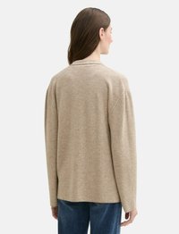 Pullover beige texturé avec une coupe décontractée, des manches longues et un col simple, associé à un jean foncé. La vue de dos montre les coutures des épaules.
