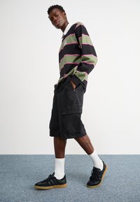 Black and gray striped long-sleeve polo shirt, green and pink stripes, paired with black cargo shorts and black sneakers with a gum sole. White socks.