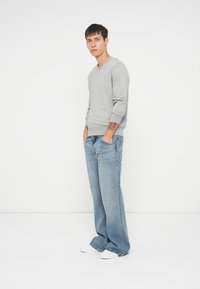 Gray v-neck sweater made of soft material, paired with light blue wide-leg jeans. Model stands with hands in pockets, wearing white shoes.