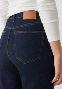 Jeans in denim blu scuro con una patch in pelle in vita, dotati di due tasche posteriori con cuciture gialle a contrasto.