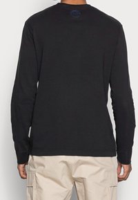 Schwarzes Langarm-T-Shirt aus Baumwolle, mit Rundhalsausschnitt und einem kleinen Logo auf dem Rücken, getragen mit beigen Cargo-Hosen.