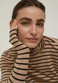 Maglione a collo alto a righe beige con strisce orizzontali nere; tessuto morbido con maniche lunghe e aderenti che mettono in risalto uno stile confortevole.