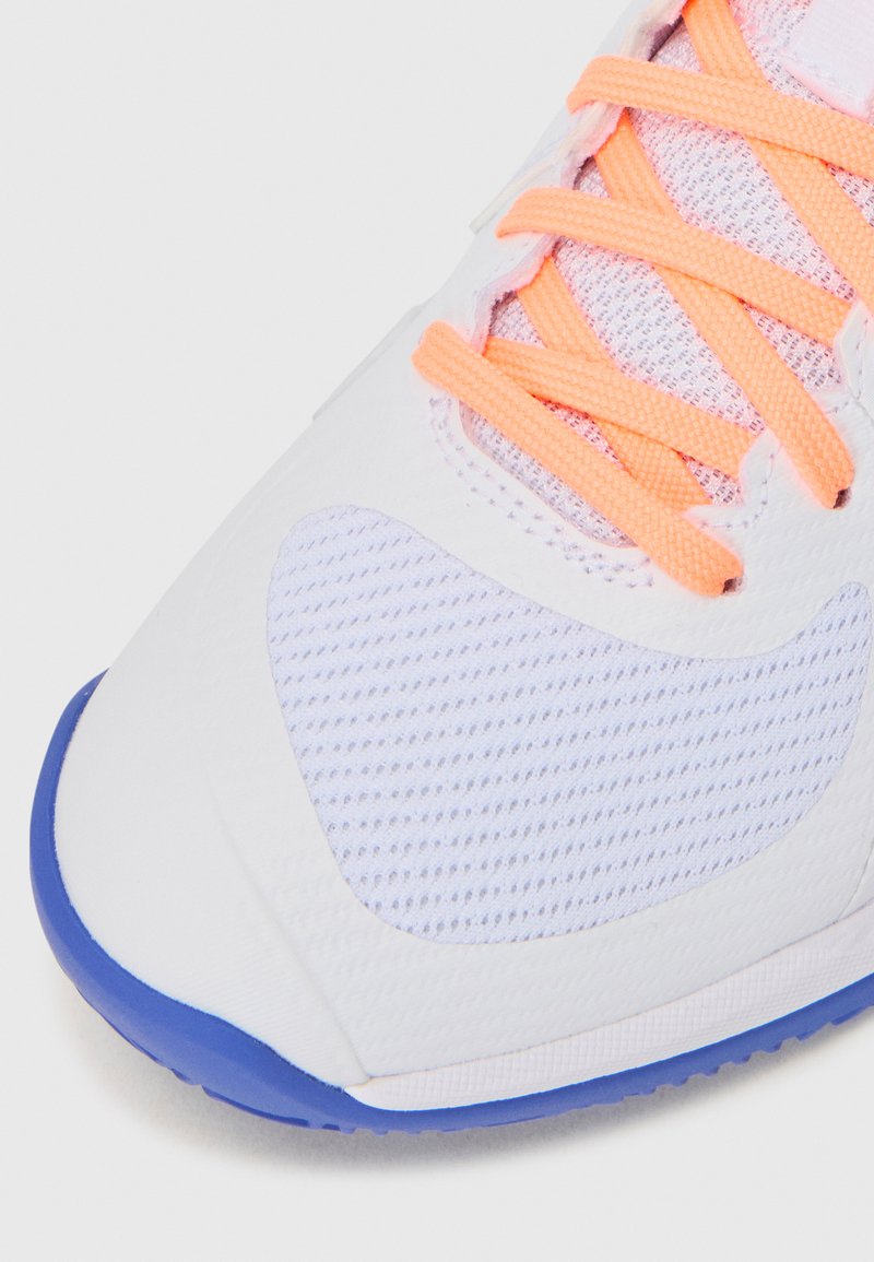White athletic shoe with mesh and textured overlays, bright orange laces, and a blue outsole. Features a streamlined design with ventilation.