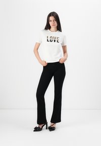 White short-sleeve t-shirt with "LOVE" in leopard print design, paired with black flared jeans and black high-heeled shoes with bow accents.