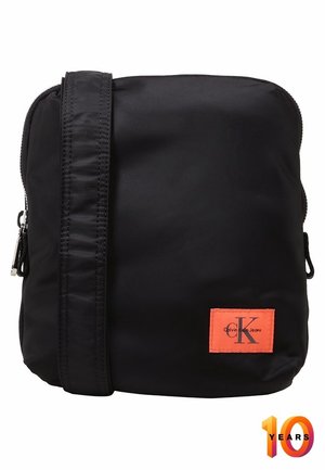 Zwarte crossbodytas met verstelbare riem en oranje Calvin Klein Jeans-logo op de voorkant.