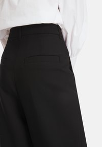 Schwarze, hochgeschnittene Hosen mit glatter Textur, ausgestattet mit zwei Gesäßtaschen und einem maßgeschneiderten Schnitt. Der Bund ist flach und elegant.