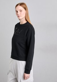 Fekete pulóver, cropped fazonban, texturált logó részlettel az elején, kerek nyakkal és rugalmas mandzsettával. Puha anyagú textúra.