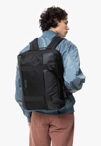 Musta reppu, joka on suorakaiteen muotoinen, jossa on pehmustetut hihnat, verkko yksityiskohtia ja useita osastoja. Käytössä henkilöllä, jolla on sininen takki.