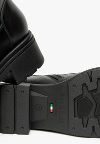 Stivaletto in pelle nera con punta rotonda, tacco spesso, suola texturizzata e soletta con marchio con colori della bandiera italiana e indicatore della taglia 37.