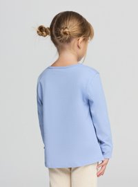 Długorękawowy T-shirt z miękkiej, jasnoniebieskiej bawełny, z okrągłym dekoltem i prostym krojem, noszony z kremowymi prążkowanymi spodniami.