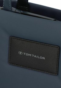 Borsa a tracolla blu navy con un'esterno liscio, caratterizzata da un'etichetta in pelle nera testurizzata con il logo "TOM TAILOR" cucito sul fronte.