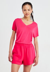Felle roze T-shirt met korte mouwen en V-hals, gecombineerd met bijpassende high-waisted shorts met voorzakken en een zachte, gladde textuur.