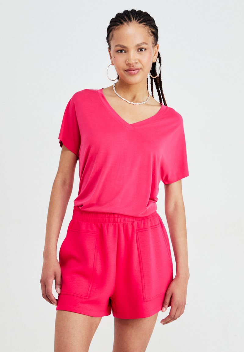 Felle roze T-shirt met korte mouwen en V-hals, gecombineerd met bijpassende high-waisted shorts met voorzakken en een zachte, gladde textuur.
