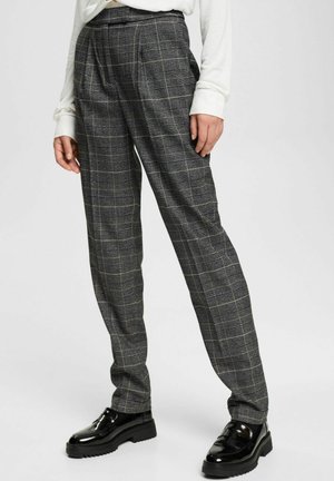 Person wearing high-waist gray plaid trousers with pleats, paired with shiny black loafers and a white long-sleeve top, standing on a plain background.