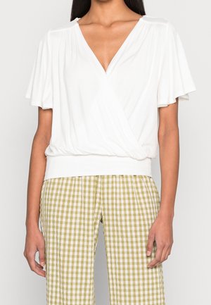 Blouse blanche à manches courtes avec col en V profond et taille froncée. Associée à un pantalon taille haute à carreaux vichy verts et blancs.