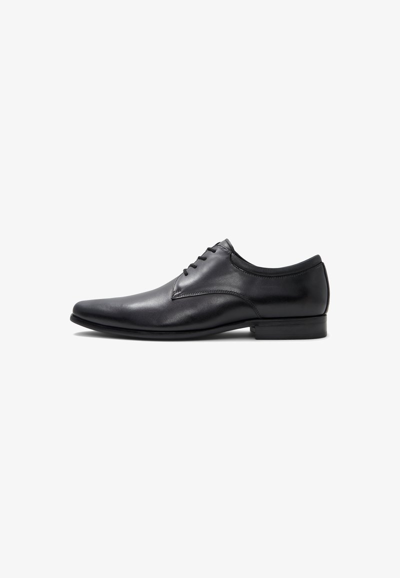 Black leather dress shoe with a pointed toe, lace-up design, smooth texture, and a low flat heel. Features minimal stitching and no patterns.