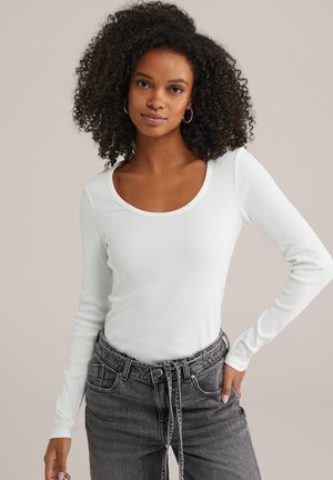 Witte langemouwen top met een ronde hals, gemaakt van ribbelstof. Gecombineerd met hoogtaille grijze jeans met een ceintuurlijn en subtiele textuur.