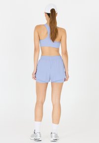 Vaaleansininen urheil bra ja yhteensopivat shortsit, jotka on valmistettu sileästä, joustavasta kankaasta. Valkoinen lippalakki, heijastavat hopeiset urheilukengät ja nilkkapituiset valkoiset sukat.