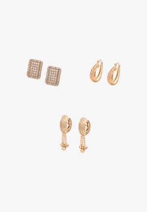 Trzy pary złotych kolczyków: prostokątne sztyfty z małymi, przezroczystymi kamieniami, teksturowane kolczyki-koła oraz teksturowane kolczyki-koła z zawieszonymi złotymi łańcuszkami z perełkami.