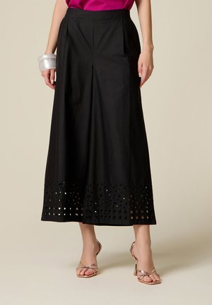 Vrouw draagt zwarte wijde cropped broek met uitsnijdingen aan de zoom, gecombineerd met metallic sandalen met bandjes en een felroze top.