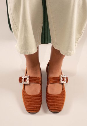 Bailarinas de pana marrón con puntera cuadrada, con detalle de hebilla decorativa. Los zapatos tienen una correa en el pie y una superficie texturizada.