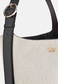 Witte geperforeerde tote bag met zwarte leren accenten en een gouden logo. Voorzien van een ronde metalen ring op de schouderband voor aanpassing.