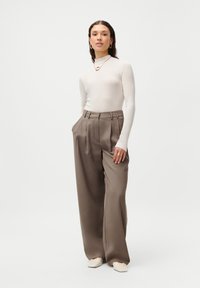 Top largo de manga larga en beige claro combinado con pantalones de pierna ancha en oliva de cintura alta. Textura suave con detalles mínimos. Zapatos de color crema.