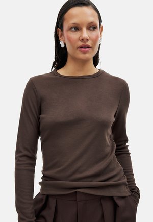 Bruine geribbelde lange mouwen top met een ronde hals, met een gladde textuur. De pasvorm sluit dicht op het lichaam en is gecombineerd met hoge taille donkere broeken.