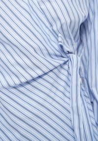 Υφασμα ανοιχτού μπλε χρώματος με λεπτές κάθετες ρίγες σε μπλε και λευκό. Διαθέτει λεπτομέρεια με στριμμένο κόμπο, απαλό υλικό και ελαφριά υφή.