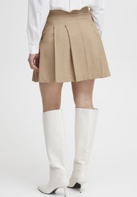 Brun plisserte skjørt med en tettsittende midje, sammen med hvite lærstøvler til kneet med spiss tå og teksturert overflate.