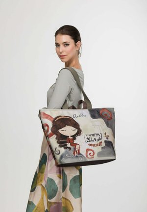 Frau trägt ein graues Oberteil und einen gemusterten Rock und trägt eine große Tragetasche mit einem Cartoon-Mädchen und dem Text "Kenne dich selbst" darauf.