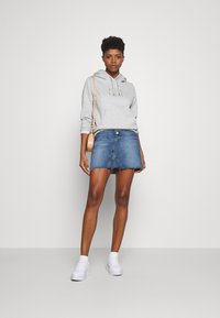 Grå huvtröja med ett framgrafik, i kombination med en blå denimminikjol med fransad fåll. Tillg ängliga vita sneakers och en beige axelväska.