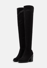 Botas negras de ante hasta la rodilla, con un tacón ancho, que presentan una cremallera lateral y una textura suave.