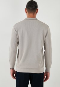 Gai pelēkā garās piedurknes polo krekls ar teksturētu audumu, ribinātām piedurknēm un apkakli. Nav redzamos zīmola vai rakstu. Rāda aizmugures skatu.