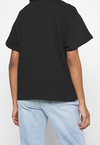 Camiseta de algodón negra con manga corta y un corte relajado. Textura suave con un cuello redondo y bordes rematados. Se lleva con jeans de mezclilla de color azul claro.