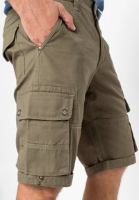 Pantaloni cargo verde oliva realizzati in tessuto resistente, con molteplici tasche, orli arrotolati e dettagli in metallo per uno stile funzionale.