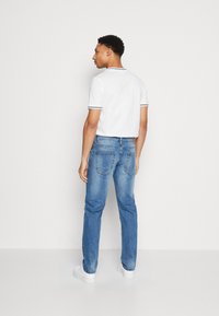 White short-sleeve polo with navy piping, paired with light blue denim jeans. Model is facing slightly to the left, wearing white sneakers.