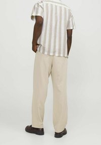 Korte mouwen gestreepte shirt in beige en wit, gecombineerd met lichtbeige losvallende broeken. Bruine schoenen maken de outfit compleet.