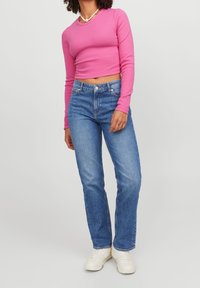 En figurnära, långärmad rosa ribbad crop top som kombineras med raka blå jeans och vita sneakers. Innehåller ett pärlhalssmycke och har ankellängd.