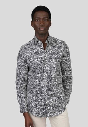 Chemise à manches longues noire avec imprimé floral blanc, col boutonné et poche poitrine. Le tissu semble léger avec une texture lisse.