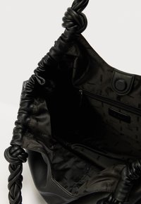 Must käekott pehme väliskatte ja palmikust sangaga. Siseosa sisaldab sileda kangaga voodrit, lukuga taskut ja bränditud logo mustrit.