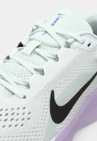 Baskets de sport gris clair avec un dessus en maille, un swoosh noir de Nike et une semelle extérieure violette, dotées de lacets et d'un col rembourré pour le soutien.