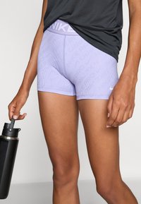 Purple Nike training shorts with a ribbed texture and logo waistband. Worn with a black top, holding a black water bottle.