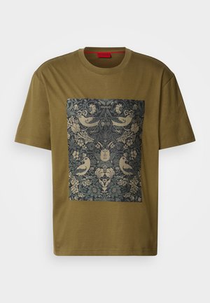 T-shirt en coton vert olive présentant un imprimé graphique rectangulaire avec des motifs floraux et d'oiseaux élaborés dans des tons de bleu foncé et d'or.