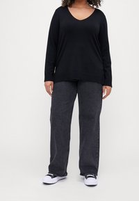 Černý dlouhý rukáv s výstřihem do V, spárovaný s volnými černými džínovými kalhotami, doplněný bílými teniskami. Hladká textury, casual design.