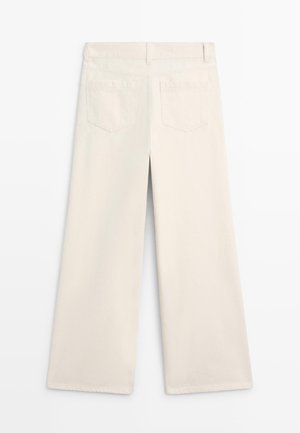 Off-white wijde broek met ceintuurlussen, twee achterzakken en zichtbare naden, plat neergelegd op een witte achtergrond.
